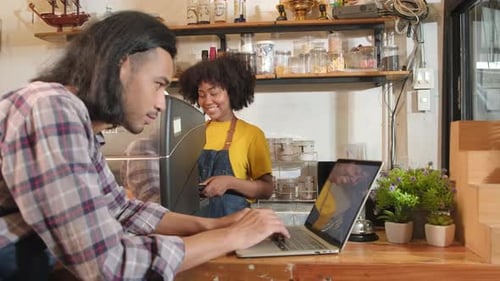 Two baristas partners talk and cheerful smile at the counter bar of coffee shop.