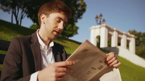 Close Up of Handsome Businessman Entrepreneur Sitting on Bench in Green Park After Work Reading