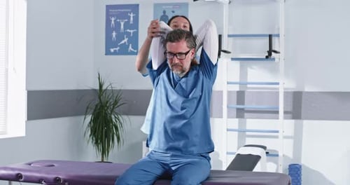 Female Rehabilitation Therapist Stretching Shoulders of Mature Patient
