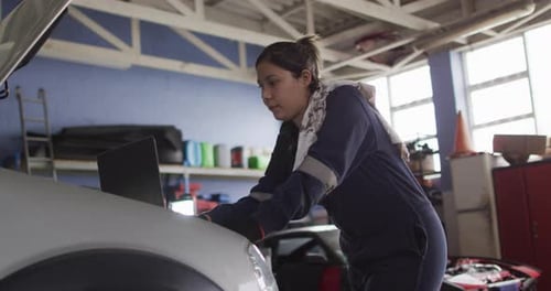 Female mechanic using laptop and inspecting the car at a car service station