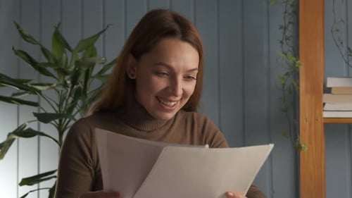Woman Celebrates Success After Reading Documents Indoors