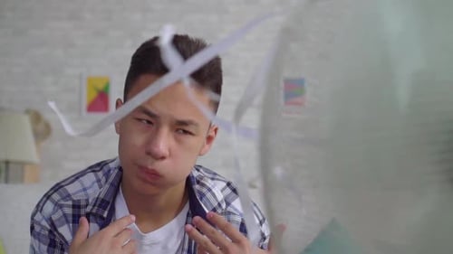 Un jeune homme asiatique sauvé de la chaleur assis devant un ventilateur en état de marche : le concept de la chaleur en gros plan
