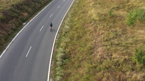 Homme à vélo en montée le long d'une route de campagne.