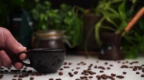 Man stellt von Hand eine schwarze Tasse heißen Kaffee oder Espresso auf einen weißen Tisch mit Kaffeebohnen darauf.