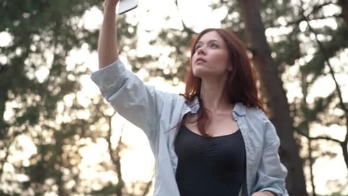 Charming Slim Woman Raising Phone Searching Internet Rejoicing in Sunshine in Forest