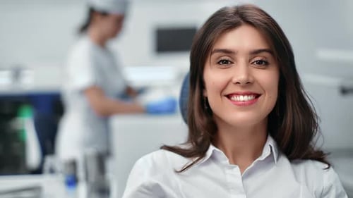 Nahaufnahme lächelnde schöne brünette junge Frau sitzt auf einem Zahnarztstuhl mit positiven Emotionen