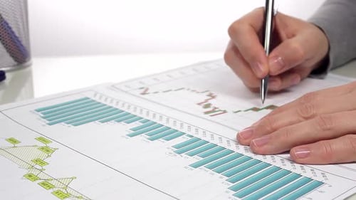 Analyzing Charts with Pen on White Desk