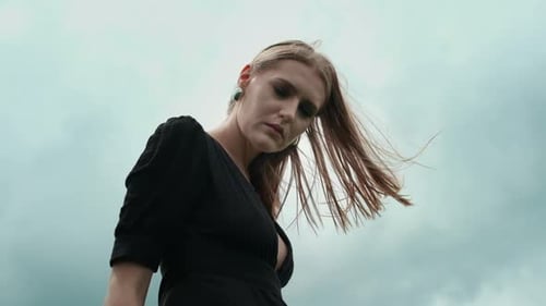 Woman in Black Dress Poses Against Cloudy Sky