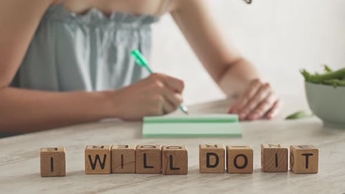 Message de motivation, slogan I Will Do It Layout From Cubes. Une jeune femme écrit dans un carnet
