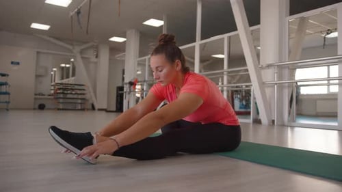 A Beautiful Young Girl Stretches in the Gym and Does Incline to the Leg While Sitting on the Mat