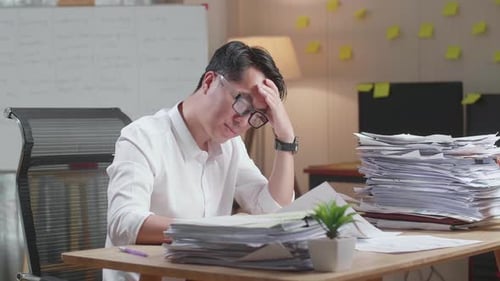 Tired Asian Man Yawning While Working Hard With Documents At The Office