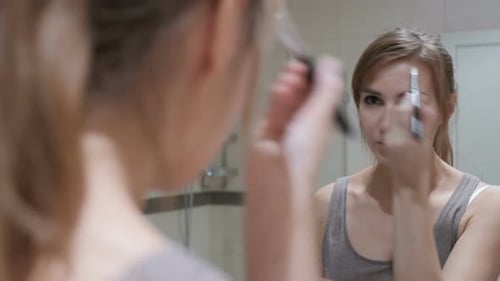 Woman Applies Makeup in Bathroom Mirror