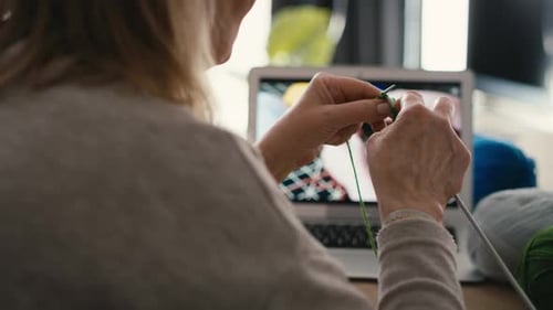 Close up of caucasian senior woman at home learning how to knit from video tutorial.