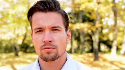 View on a Young Handsome Man Who Looks Serious, Stare Into Camera and Stands in the Park
