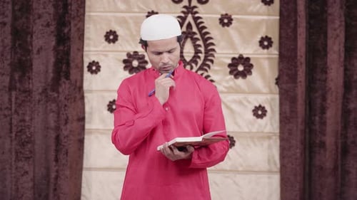 Man Writing in Book Wearing Prayer Cap