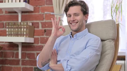 Man Gives OK Gesture While Sitting in Chair