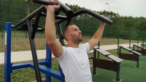Young Man Trains Outdoors on a Sunny Summer Day Trains His Shoulders on a Simulator in the Park