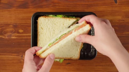 Hands Positioning Salmon Sandwich on a Black Tray
