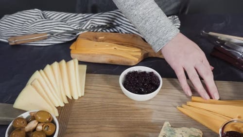 Arranging gourmet cheese, crakers, and fruits on a board for a large cheese board.