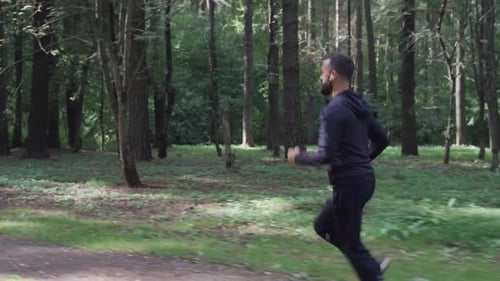 Man Running Through Summer Forest Camera Following Runner in Wireless Headphones Healthy Lifestyle