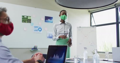 African american woman wearing face mask giving presentation to her colleagues at modern office