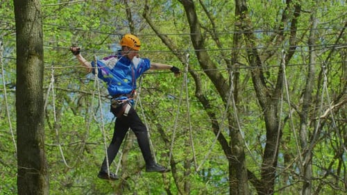 Man Carefully Crosses Rope Bridge Course in Forest