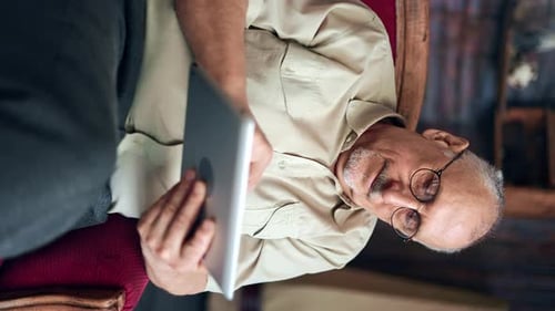 VERTICAL VIDEO POV Smiling Elderly Man Browsing Internet Clinic Application Use Tablet Relaxing