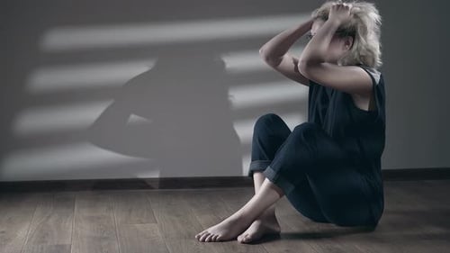 Blonde Woman Sitting on Floor with Hands on Head