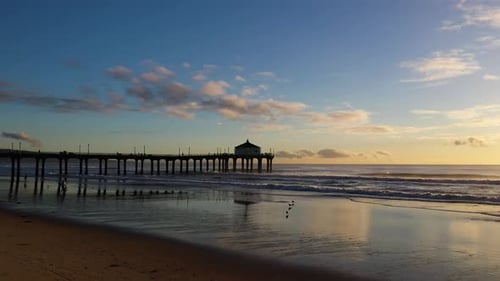 Aerial view of Manhattan Beach Pier, California, with waves crashing on the sandy shoreline, at suns