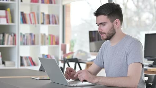 Young Man with Laptop Smiling at Camera in Office