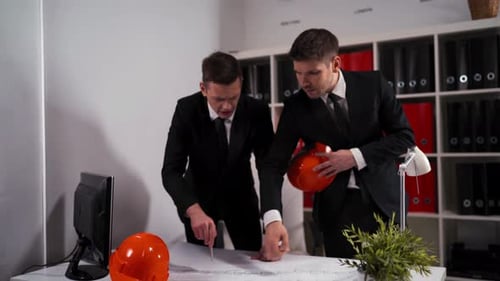 Zwei Ingenieure Geschäftsleute im Geschäftsbüro betrachten Architektenzeichnung mit Helm
