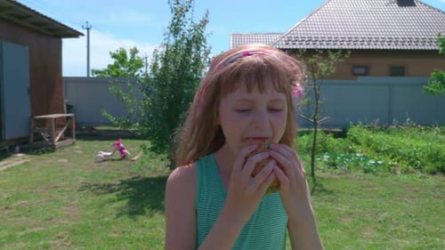 Girl Eating Burger Outdoors in Yard on Sunny Day