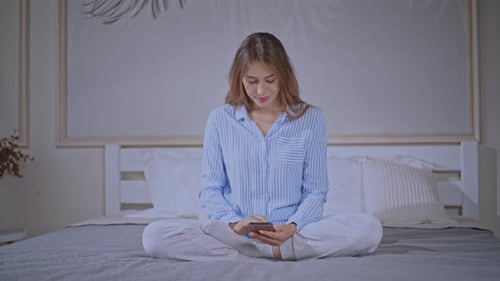Young Woman Using Smartphone on Bed at Home