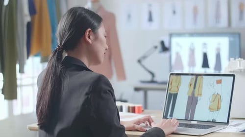 Vista posterior de una diseñadora asiática en traje de negocios diseñando ropa en una computadora portátil en el estudio