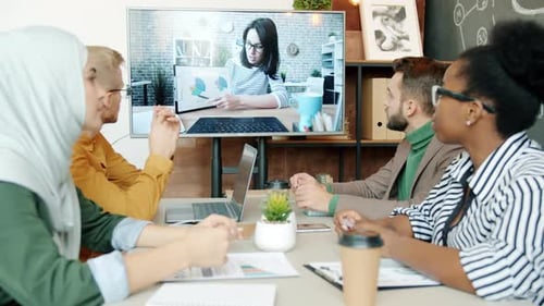 Gruppe von Geschäftsleuten diskutiert Projekt mit einer Kollegin per Videoanruf