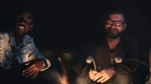 Friends roasting marshmallows around campfire at night
