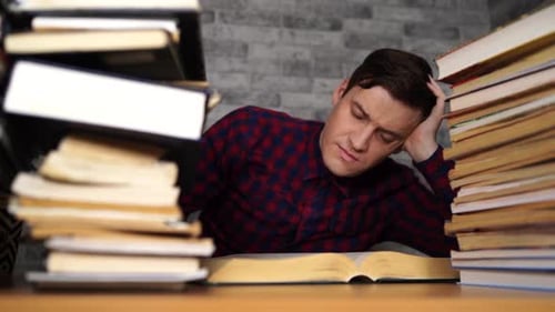 Man Student Boring Reading Book at Library with a Lot of Books in University.