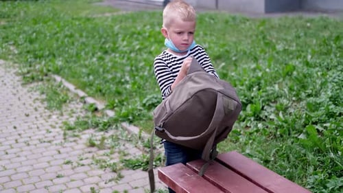 Caucasian Boy in Striped Tshirt Puts Mask on His Face and Backpack on Back and Goes to School on