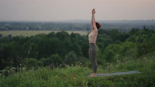 Woman Practicing Yoga on Grassy Hillside
