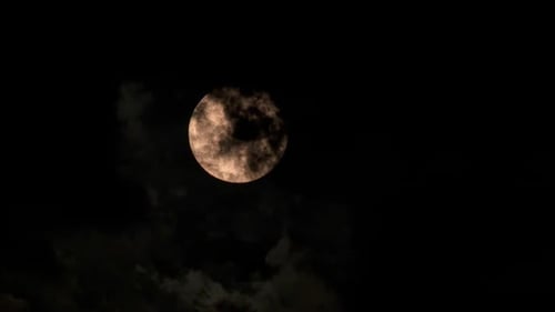 Glowing Full Moon Rising Through Dark Cloudy Sky