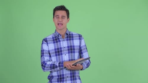 Glücklicher junger gutaussehender Hipster-Mann spricht bei der Verwendung eines digitalen Tablets