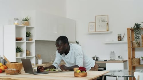 Young Adult Works on Laptop While Eating Salad