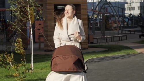 Portrait of Smiling Woman with Baby in Pram or Stroller Walking in Park on Windy Day