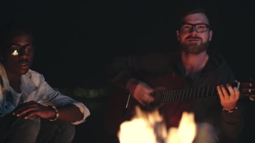 Friends Gather Around Campfire at Night with Guitar