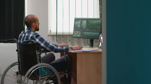 Man in Wheelchair Working at Desk on Computer