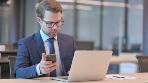 Man Using Phone with Laptop in Office