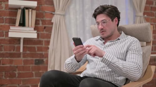 Excited Man Celebrates Success on Smartphone Indoors