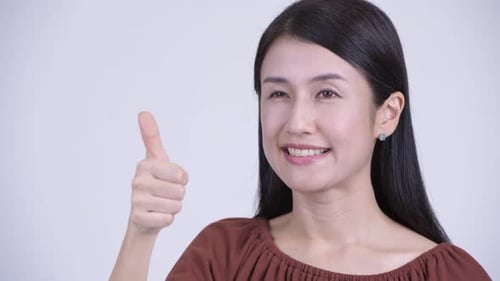Gesicht einer glücklichen schönen asiatischen Frau, die Daumen hoch gibt