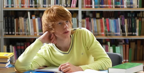 Young Man Studying in Library Writes in Notebook