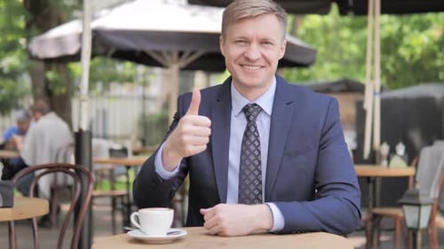 Thumbs Up By Businessman Sitting in Outdoor Cafe